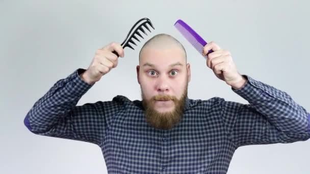 Der Mann mit der Glatze kämmt seine Glatze mit zwei Kämmen und blickt in die Kamera — Stockvideo