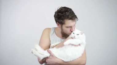 Sakallı hippi adam elinde kocaman beyaz bir kedi tutuyor.
