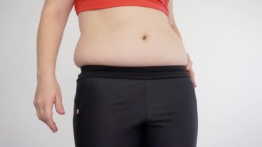 Spor giyimli şişman bir kadın göbeğini çimdikliyor. Selülit ve aşırı yeme