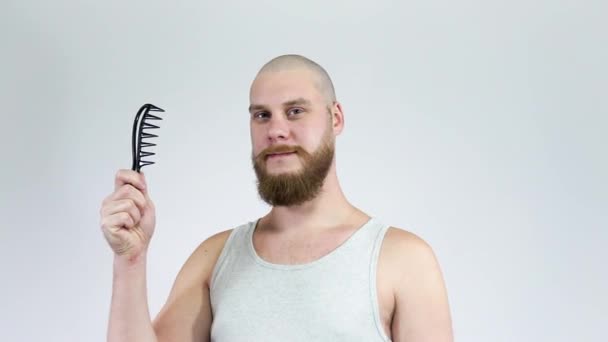 O careca com a barba arbustiva posa para a câmera segurando um pente — Vídeo de Stock