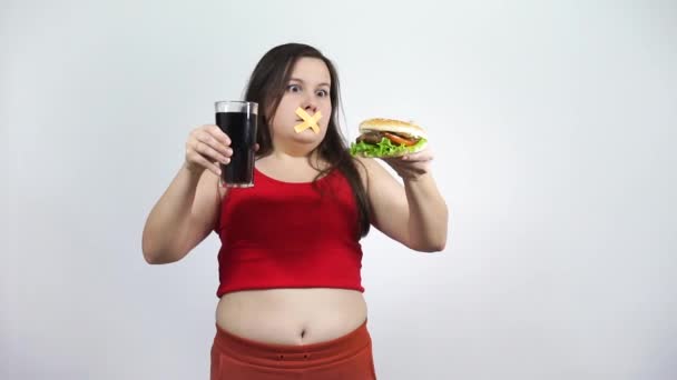Een meisje met een getapete mond op zoek naar een hamburger.Je mag geen junk food eten. — Stockvideo