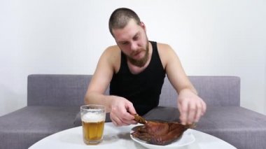 Genç adam kanepede oturmuş bira içiyor ve kurutulmuş balık yiyor..