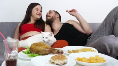 Kalın kız ve bir adam TV izler ve fast food yer. Farklı gözlü beyaz kedi..