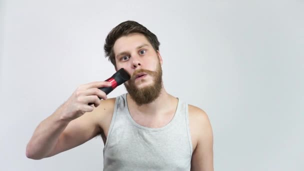De baard verzorgen. De man knipt zijn baard met tondeuses in de badkamer. — Stockvideo