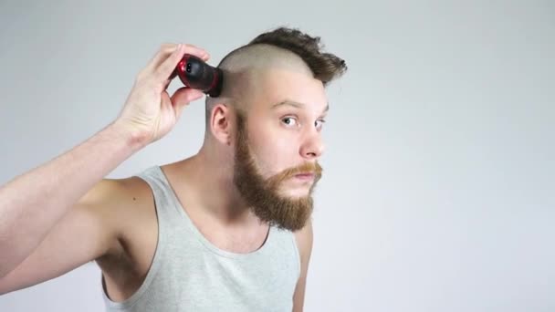 De man scheert zijn hoofd met tondeuses voor een spiegel.Kaal en een baard. — Stockvideo