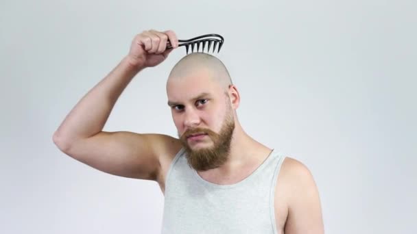 Bald young man with a beard combing his bald head with a comb and cries — Stock Video