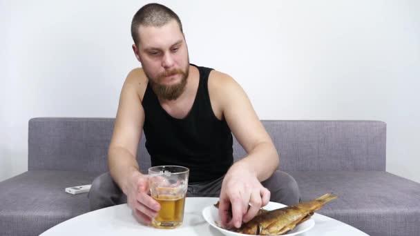 Man tittar på TV och dricker öl med fisk.Ensamhet och alkoholism. — Stockvideo