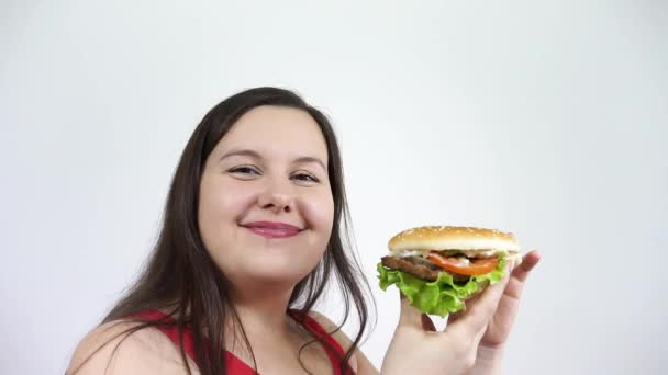 En ung kvinna med fetma att äta en hamburgare och känna glädjen.Snabbmat, skräp. — Stockvideo