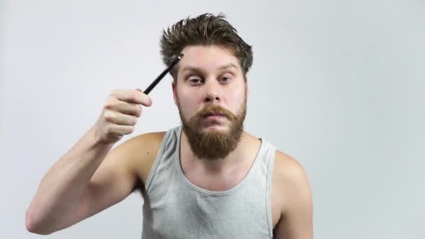 Бородатий хлопець розчісує волосся і дивиться у дзеркало . — стокове відео