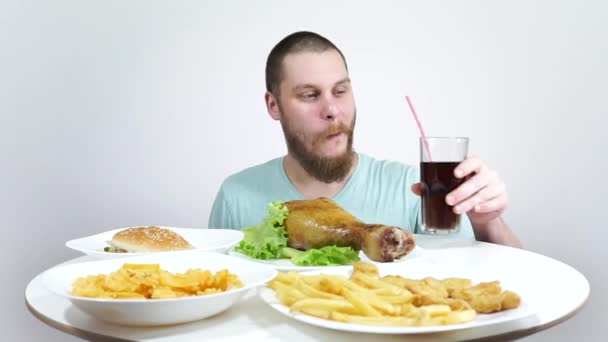 L'homme à la table plein de fast food, mangeant un hamburger et buvant un coca . — Video