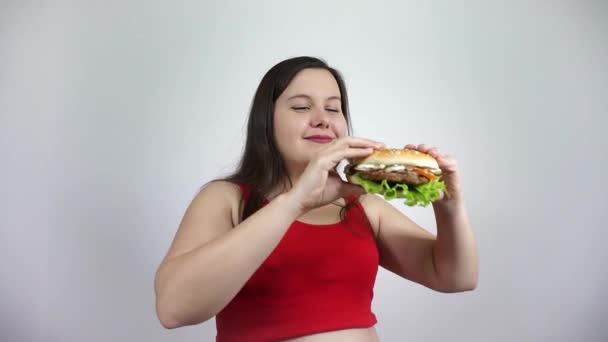 Menina gorda comer um hambúrguer. Mulher com excesso de peso em vermelho comer fast food.Obesity . — Vídeo de Stock