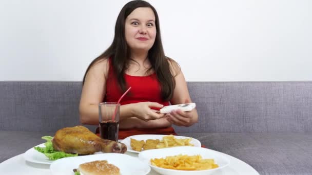 Chica gorda con vientre comiendo pollo frito y viendo la televisión . — Vídeo de stock