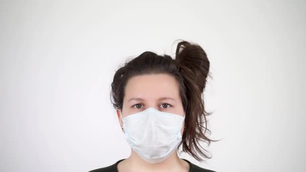 A koronavírus járvány. Egy fiatal nő orvosi maszkban a kamerába néz.. — Stock videók