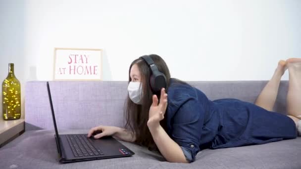Дівчина працює на ноутбуці в масці. Залишайтеся вдома — стокове відео