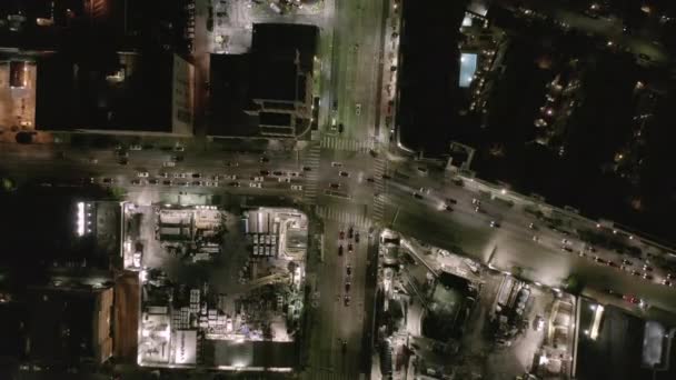 AERIAL: Ascensão aérea na rua de interseção com grande canteiro de obras e buracos no chão à noite com ruas brilhantes e luzes de trânsito da cidade — Vídeo de Stock