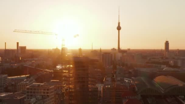 АЭРИАЛ: Берлин, Германия, строительная площадка с кранами с красивым закатом, солнечным светом и видом на Алексиевскую телебашню, солнечные батареи — стоковое видео