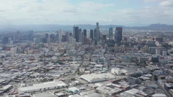 AERIAL: Círculo lento en el centro de Los Ángeles Skyline con Warehouse Art Distrct en primer plano con cielo azul y nubes — Vídeos de Stock