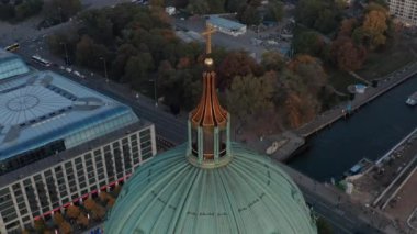 Berlin Katedrali 'nin tepesinde altın haç ve arka planda sokaklar Almanya' nın sonbahar renkleriyle güzel günbatımında daireler çiziyor.