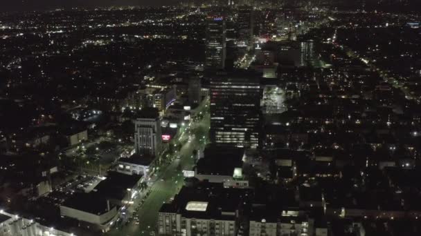 AERIAL: Sobre Wilshire Boulevard em Hollywood Los Angeles à noite com ruas brilhantes e luzes de trânsito da cidade — Vídeo de Stock