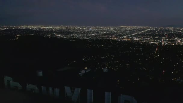 AERIAL: Spektakulärer Dolly über Hollywood-Schild bei Nacht mit Lichtern von Los Angeles City — Stockvideo