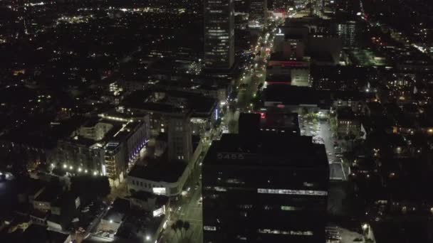 AERIAL: Sobre Wilshire Boulevard en Hollywood Los Ángeles por la noche con calles brillantes y semáforos de coches urbanos — Vídeo de stock