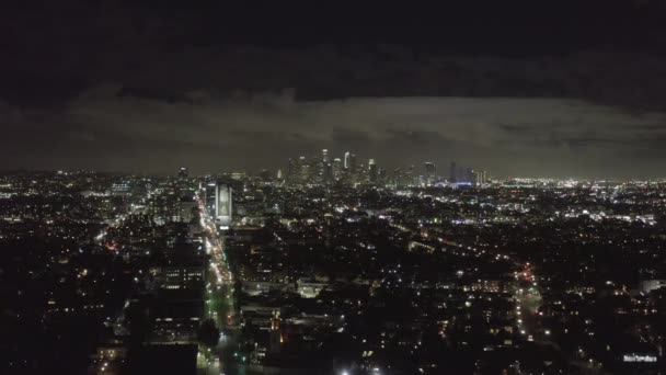 AERIAL: Sobre Dark Hollywood Los Angeles por la noche vista en Wilshire Blvd con nubes sobre el centro y City Lights — Vídeos de Stock
