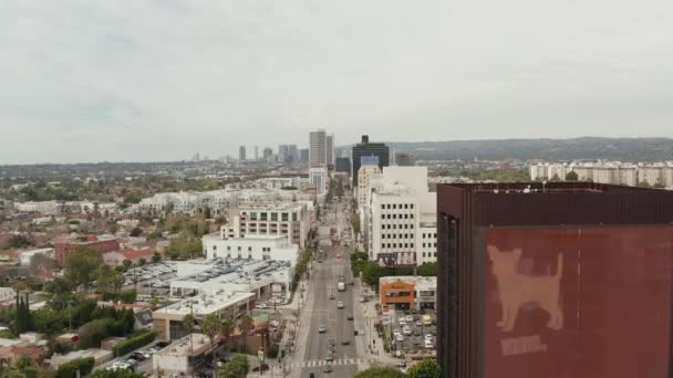 АЭРИАЛ: Полет над Уилширом Фабрегасом рядом с улицей и зданиями с автомобильным трафиком в Лос-Анджелесе, Калифорния в пасмурный день — стоковое видео