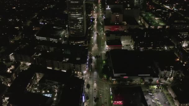 AERIAL: Sobre Wilshire Boulevard en Hollywood Los Ángeles por la noche con calles brillantes y semáforos de coches urbanos — Vídeos de Stock