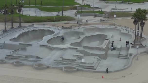 АЕРІАЛ: поверніть навколо Венеціанського пляжного скейтпарку з велосипедами і пальмами вранці, Cloudy Los Angeles, California — стокове відео