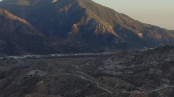 AERIAL: Ao longo da Califórnia Country Side com rodovia e montanhas ao pôr do sol — Vídeo de Stock