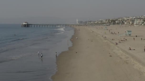AERIAL: Gente en las olas de la playa, agua con muelle en Los Ángeles, California, soleado, cielo azul — Vídeo de stock