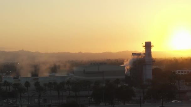 AERIAL: gőzölgő gyár pálmafákkal és forgalmas autópályával Burbankben, Los Angelesben, Kaliforniában, naplementében — Stock videók