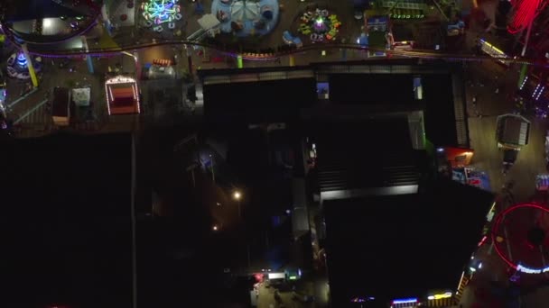 AERIAL: 페리스 휠 과 형형색색의 조명을 받으며 밤에 산타 모니카 부두에서 경치를 감상하는 모습, — 비디오
