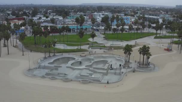 AERIAL: Käänny ympäri Venice Beach Skatepark pyöräilijöiden ja palmujen aamulla, Cloudy Los Angeles, Kalifornia — kuvapankkivideo