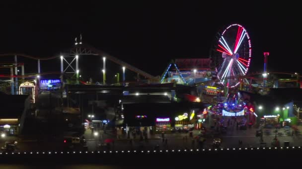 AERIAL: Vista lateral del muelle de Santa Mónica por la noche con noria y luces de colores , — Vídeo de stock