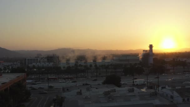 AERIAL: Fábrica de vapor con palmeras y autopista ocupada en Burbank, Los Ángeles, California, puesta del sol — Vídeo de stock