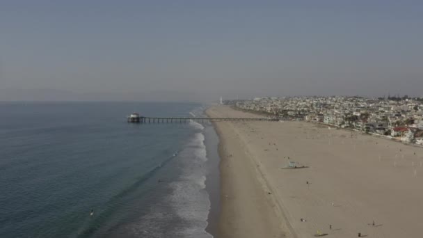 AERIAL: Människor vid strandvågorna, vatten med brygga i Los Angeles, Kalifornien, Sunny, Blue Sky — Stockvideo