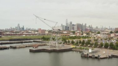Rıhtımlarda endüstriyel vinçler arasında uçarken New York City arka planda ve nehirde ufuk çizgisi 