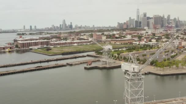 AERIAL: Grúa industrial circular en muelles con horizonte de la ciudad de Nueva York en el fondo y el río — Vídeo de stock