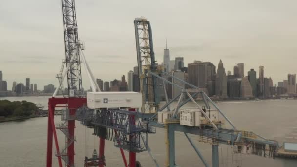 AERIAL: Close-up van industriële kranen in dokken met New York City met skyline op achtergrond en rivier — Stockvideo