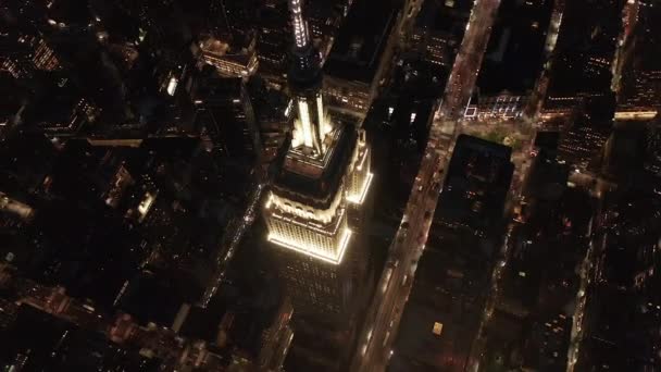 AERIAL: Círculo de tirar o fôlego sobre o icônico Empire State Building acima iluminado avenidas paralelas e junções condomínios residenciais e edifícios de escritórios no centro de Manhattan, Nova York à noite — Vídeo de Stock