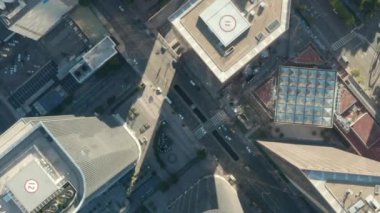Helikopter, Los Angeles şehir merkezindeki gökdelenlerin çatıları ve araba trafiğinin önünden geçerken, Los Angeles 'ın aşağısına doğru yavaşça iniyor ve daire çiziyor. 