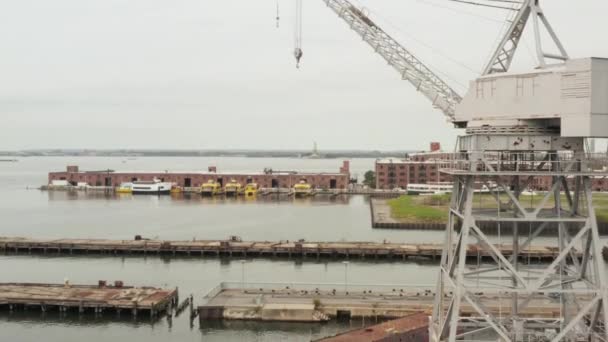 AERIAL: Flug unter Industriekränen in Docks mit Blick auf die Freiheitsstatue in New York City und den Fluss — Stockvideo