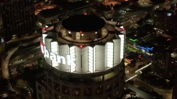 AERIAL: Närbild av US Bank Tower skyskrapa och Downtown Los Angeles, Kalifornien på natten, glödande stadsljus med motorväg i bakgrunden — Stockvideo