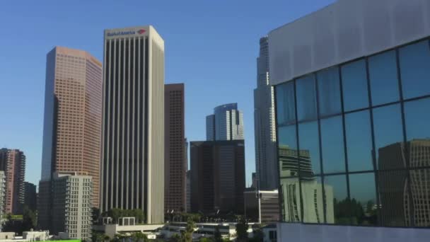 AERIAL: Revelação do centro de Los Angeles, Califórnia Skyline por trás do edifício com janelas de vidro no céu azul bonito e dia ensolarado — Vídeo de Stock
