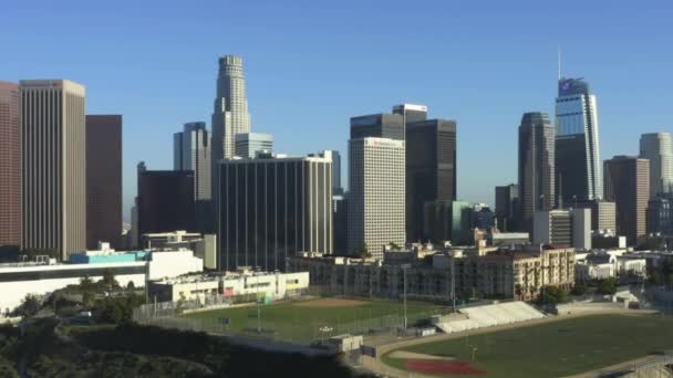 AERIAL: Repülés felé Downtown Los Angeles, California Skyline sport labdarúgó baseball és teniszpálya gyönyörű kék ég és napos nap — Stock videók