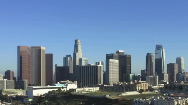 AERIAL: Flying to Downtown Los Angeles, California Skyline with sports football baseball and tennis field at pretty blue sky and sunny day — стокове відео