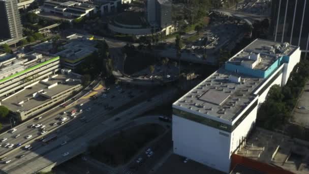 AERIAL: Centrum Los Angeles, Kalifornie křižovatka provozu s palmami a Skyline v pozadí na krásné modré obloze a slunečný den — Stock video