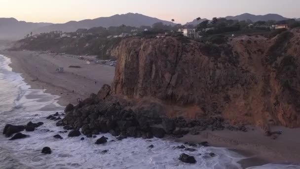 AERIAL: repülés Malibu felett, Kalifornia kilátás a strandra Shore Line Paficic óceán naplementekor hegyi sziklával — Stock videók