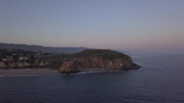 Malibu, California 'da sahil şeridi manzaralı Paficic Okyanusu üzerinde gün batımında dağ yamacıyla uçmak